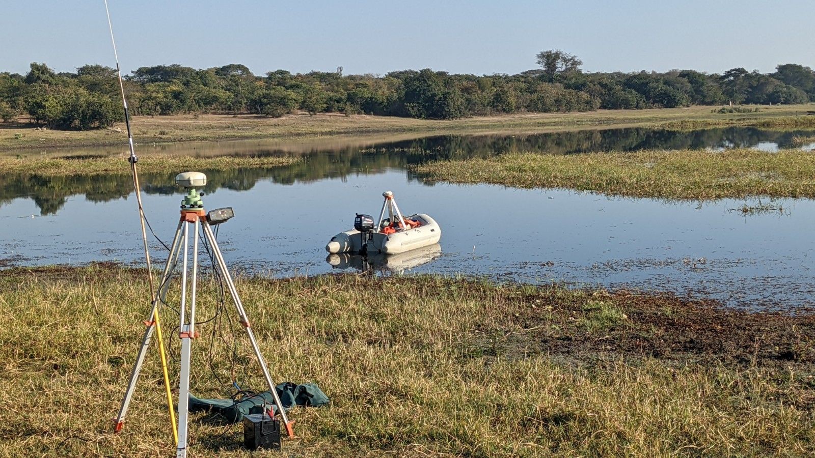 Survey boat on a reservoir with a base station set up on the shore